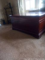 Photo showing front and side of the reddish-brown wooden cedar chest with paneled sides.