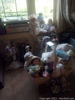 Wide view of dolls arranged on the floor and window sill, showing teddy bears in basket and multiple dolls in Victorian style dresses.