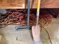 Photo of extension cords, shovel, garden cultivator, floor seen with dirt and wood walls