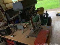 Delta drill press on wooden workbench, accompanied by a red toolbox and other workshop items.