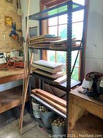 Metal shelving unit in a workshop or shed holding wood planks and other materials, showing overall condition and contents