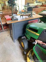 Full view of workshop cabinet with wooden top and red metal drawers under the work surface, placed next to a John Deere lawn tractor.