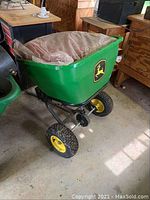John Deere green lawn seeder with yellow wheels and a plastic lining inside.