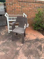 Photo showing the brown plastic chair positioned in front of the white plastic serving cart on wheels, placed on a patio next to a brick wall and bush.