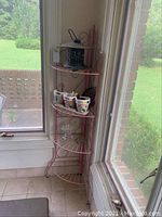 Full view of pink metal corner shelf with assorted items on shelves.