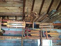 Four vintage wooden sleds hanging from ceiling in a rustic storage area, shows different brands and designs of sleds with wooden slats and metal runners.