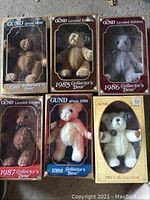 Six Gund collector bears in original boxes, arranged close together on ground showing front of boxes and bears inside. Bears are from 1984 to 1989, each box labeled with year and edition.