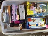 Top-down view of six boxed Barbie dolls in plastic bin
