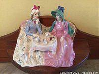 Front view showing two women seated having tea on a loveseat, porcelain glossy finish with pastel colors.