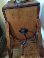 Photo of the wooden vintage hand-crank grinder showing the metal crank and wooden handle, supported by wooden legs and reinforced with metal corners.