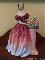 Front view of Royal Doulton Roseanna figurine in red and white gown holding a flower bouquet on a pedestal.