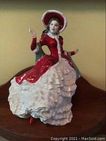 Front and side view of Royal Doulton Victorian Christmas HN4625 porcelain figurine dressed in red and white with bonnet and blue mantle.