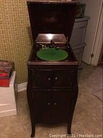 Front view of open wooden phonograph cabinet showing green felt turntable and lower storage doors.