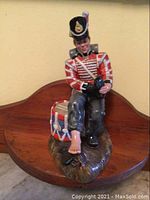 Front view of Royal Doulton Drummer Boy figurine seated on a stump with detailed red and white uniform, drum, and bare foot visible.