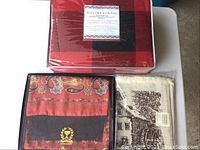 Image showing entire lot with all three boxed items: the red and black queen duvet set, a red and black patterned textile, and a neutral house and tree design textile.