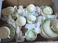 Overall view of various Grindley china pieces in a box, including cups, saucers, and plates wrapped in tissue paper.