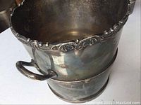 Silver serving bucket showing floral edge, side handle, tarnished surface