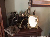 Photo showing collection of antique metal bells, a yellow brass mirror, and metal bugle horn arranged on wooden surface.