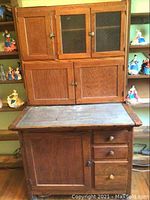 Front view of entire antique Hoosier cabinet showing two-tier design, metal countertop, storage compartments and drawers.