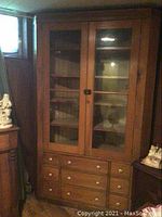 Full view of large wooden corner cabinet showing glass doors and drawer section.