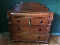 Front view of a vintage hardwood dresser with three drawers, black knobs, and decorative carved back detail