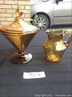 Side view of amber glass covered candy dish and diamond pattern pitcher with car in background