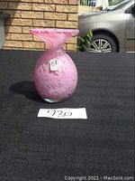 Photo showing front angle of pink swirl Mdina glass vase on black surface with a car and brick wall background