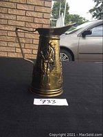 Side view of brass pitcher showing man figure embossed in front, under handle