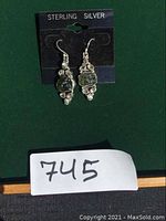Front view of the sterling silver earrings with moldavite and herkimer diamond stones on display card labeled sterling silver.