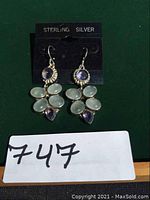 Front view of the pair of sterling silver earrings showing amethyst and moonstone stones set in a silver floral design with ear wires on black card.