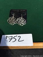 Pair of sterling silver rose-shaped earrings on a black display card labeled 'STERLING SILVER' photographed from front view on a green background.