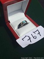 Front view of abalone shell ring inside red jewelry box with white interior, showing iridescent shell inlay and polished metal band. Lot tag '767' present.