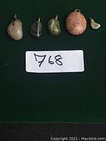 Five assorted stone pendants arranged side by side on a dark green surface, each with a metal loop for attaching to a necklace.
