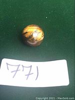 Front view of polished tiger eye sphere on green background with lot number card 771