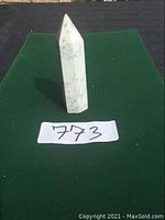 Full view of the white marble crystal point on a green cloth background, showing its height, shape and natural veining.