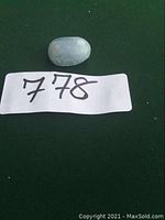 Single polished celestine tumbled rock on dark green background with lot number 778.