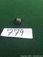 Small black tumbled jet stone on green background with lot number 779 marker.