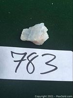 Photo of a rough blue calcite stone angled showing light blue and beige mineral textures on a dark green background with the number '783' near the bottom
