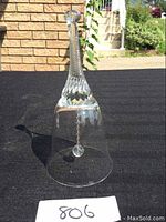 Clear crystal bell upright on black fabric, highlighting the textured handle, smooth bell body, and the internal crystal clapper.