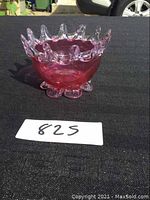 Side photo showing ruby red glass bowl with clear crown rim and round clear base on black surface.