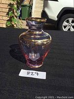 Front and side view of the purple blown glass vase sitting on a black cloth background with sunlight highlighting the gold decoration and translucent purple glass.
