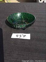 Dark green blown glass bowl shown on black fabric background for scale. Photo taken from a side angle.