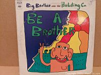 Front cover art of "Be A Brother" vinyl album by Big Brother and the Holding Company showing cartoon illustration with colorful background.