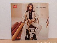 Front cover of Eric Clapton vinyl album showing him seated with electric guitar.