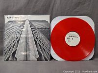 Front cover of The Darcys AJA album and red vinyl record outside its sleeve