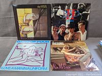 Four vinyl records in their cover sleeves arranged on a table, showing front covers for The Fixx, Big Audio Dynamite, Gang of Four, and The Higsons.