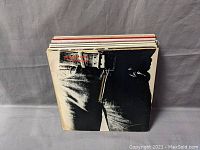 Photo of stack of vinyl records showing album cover with jeans and belt, likely Rolling Stones' Sticky Fingers album cover