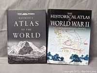 Front covers of two large atlas books side by side on a grey fabric surface