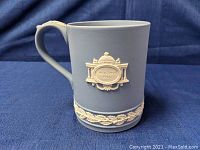 Side view of blue Wedgewood jasperware mug with white relief decoration labeled Christmas 1975, showing detailed design and handle.