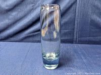 Clear glass vase with a cylindrical shape, shown against blue fabric background.